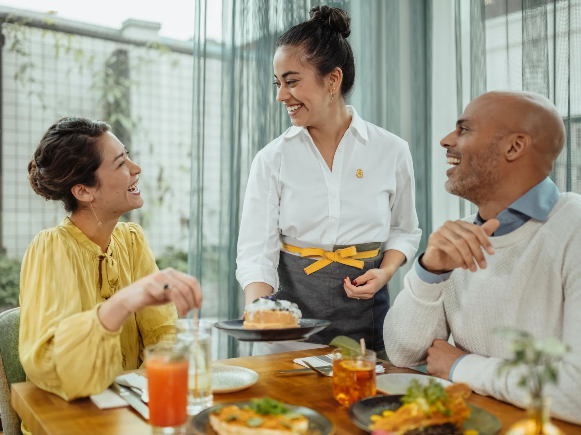 A server laughs with the couple at the table surrounded with delicious foods