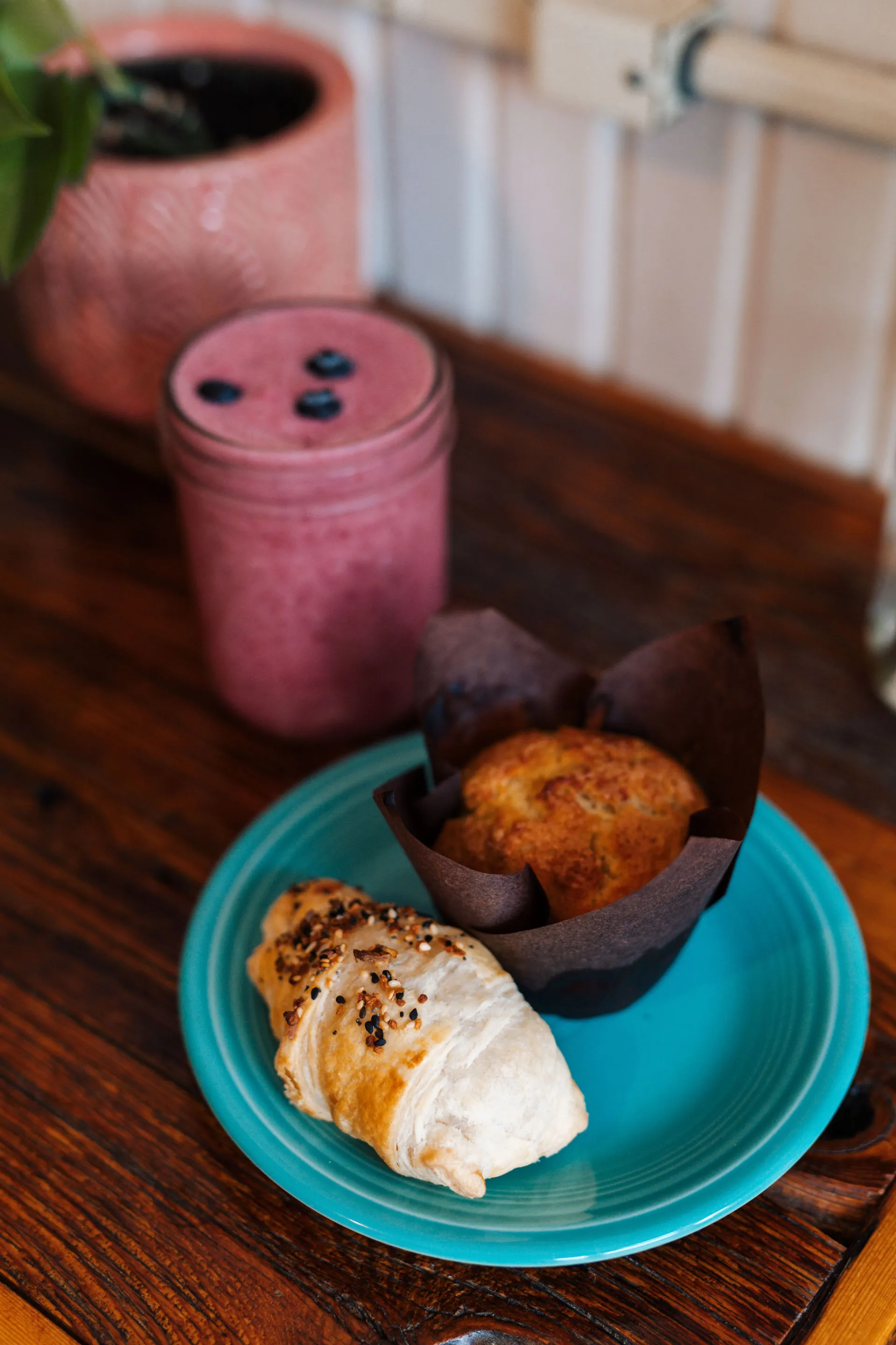 Muffin and croissant on a plate next to a berry smoothy.