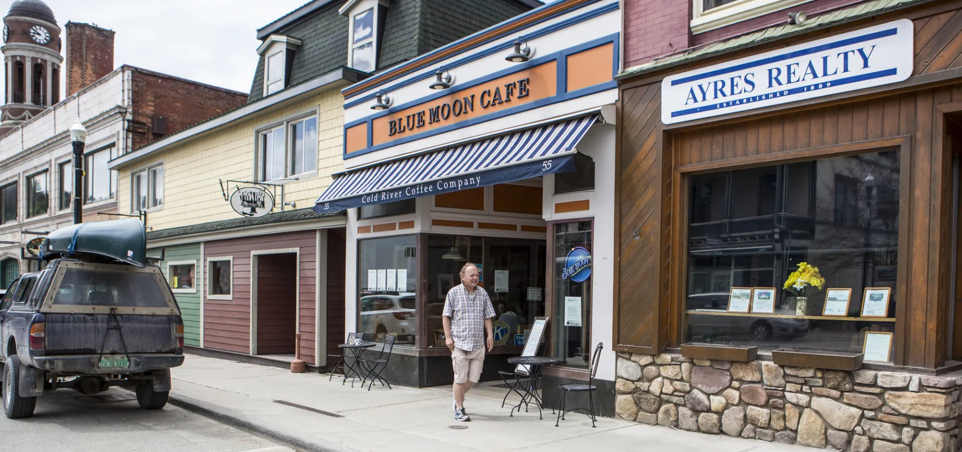 A man walks out of a cafe onto a main street. 