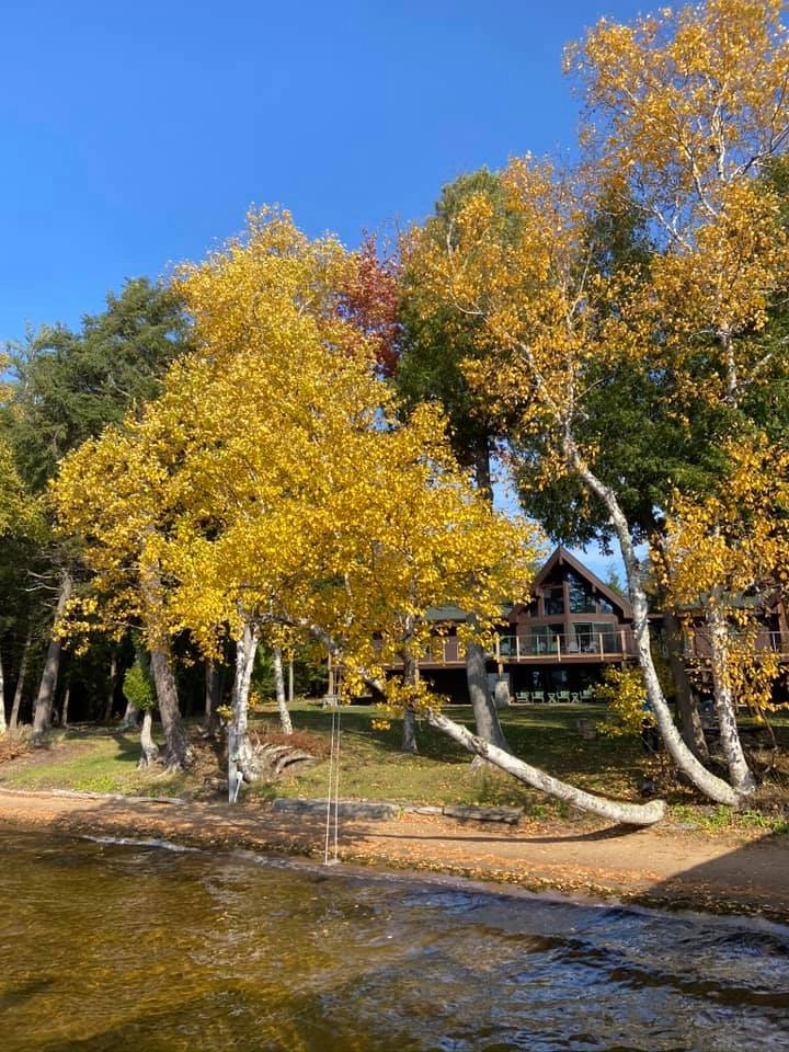 Fall view of the Alpenglow Lakeside Lodge from the dock showing all the vibrant foliage against the blue sky.