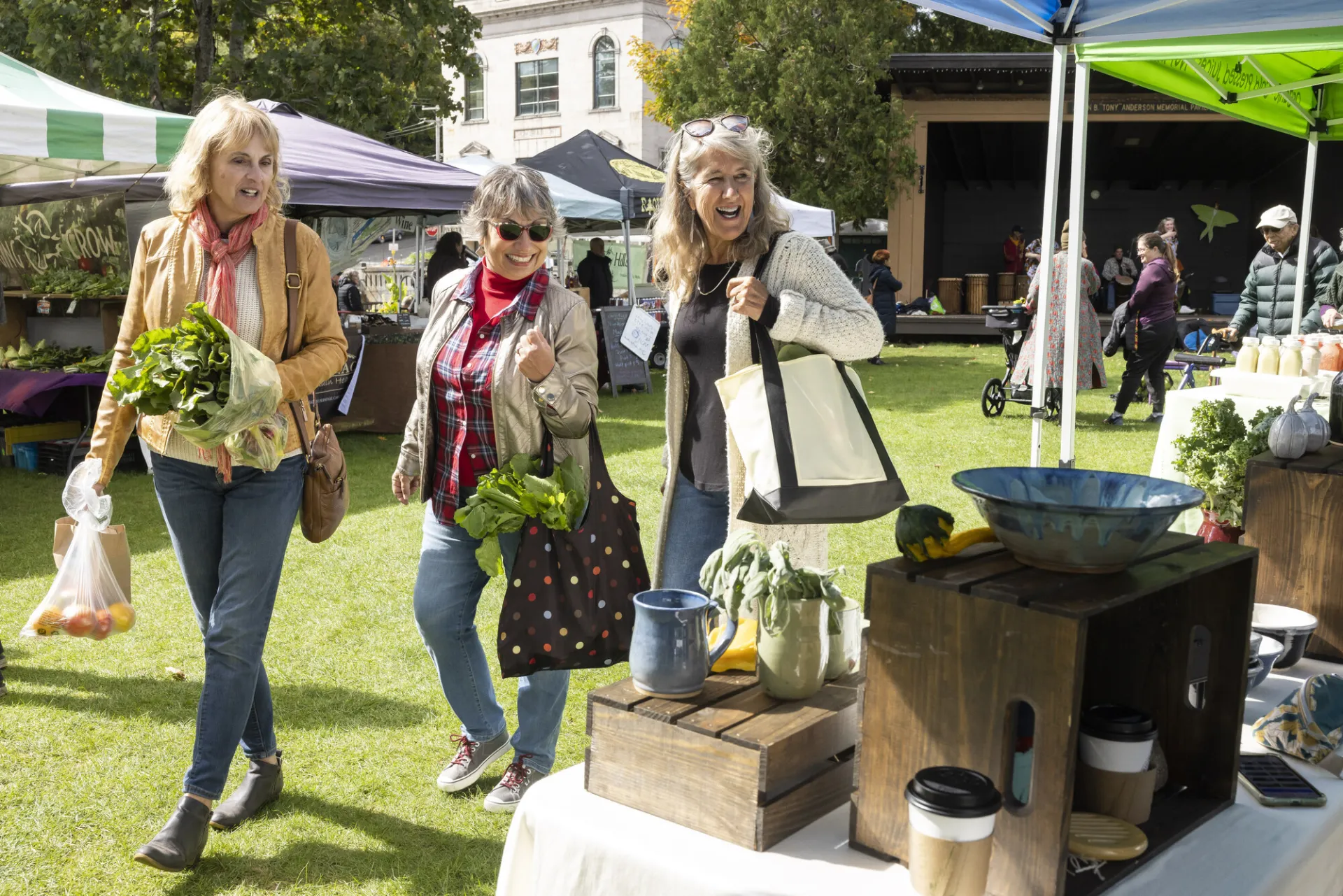 Three women walk around a farmers market in a park. 