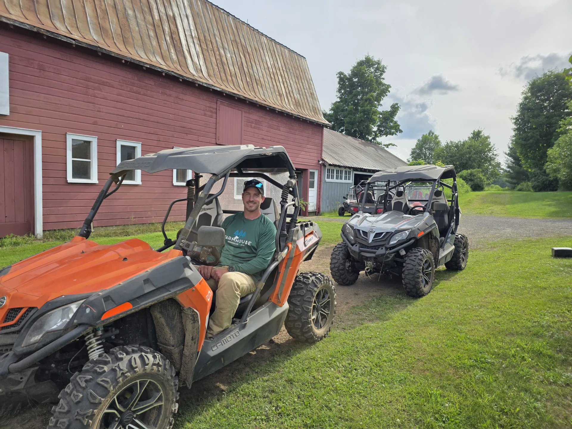 Man sitting in an orange UTV in front of Red Barn. 