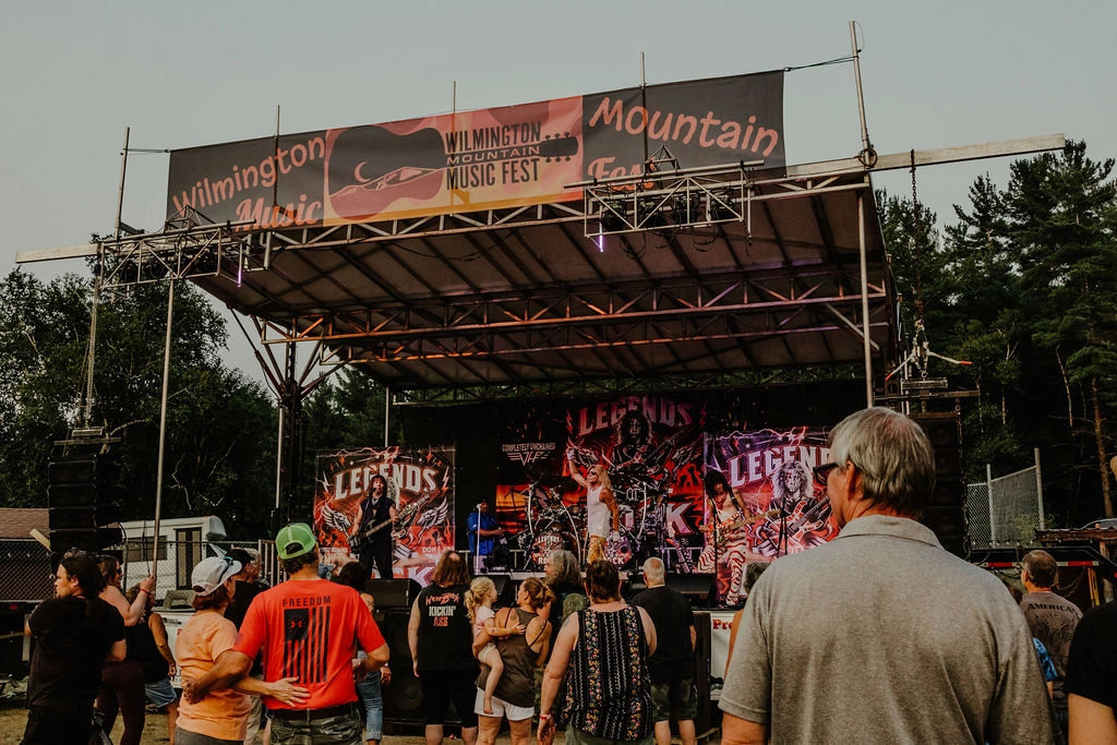 Crowd of people stands looking at music festival stage outdoors in summer