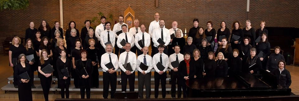 The mens choir stands on stage with white shirts, black ties and pants.