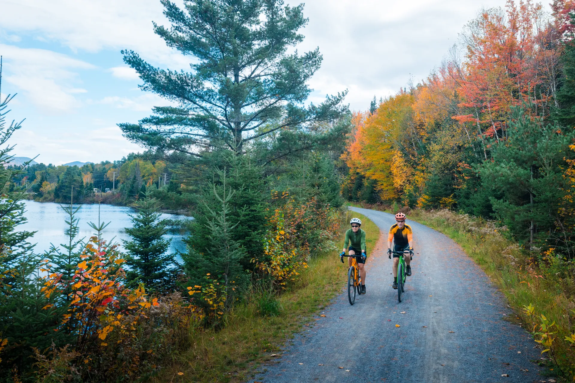 A man and woman cycle on a fall path along a lake.