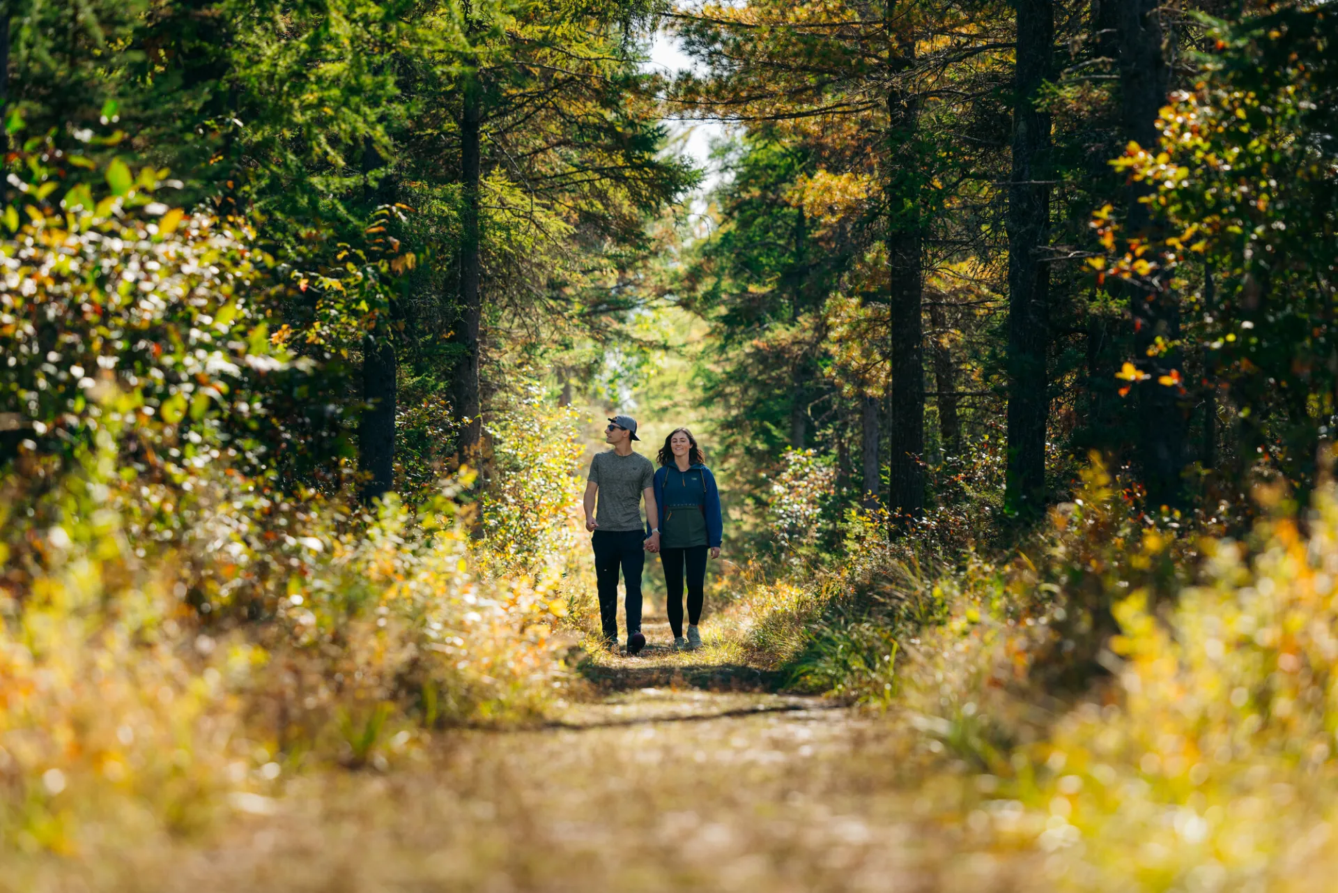A man and woman walk on a trail in fall surrounded by wild flowers.