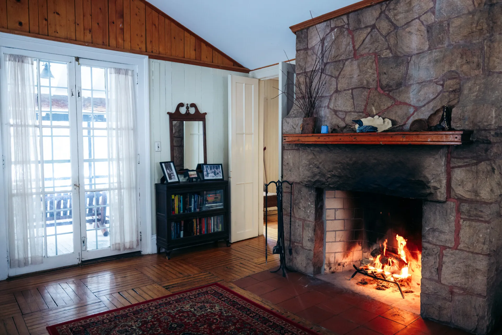 A vacation rental living room shows a roaring fire in a stone fireplace, antique furniture, and a softly-lit French door.