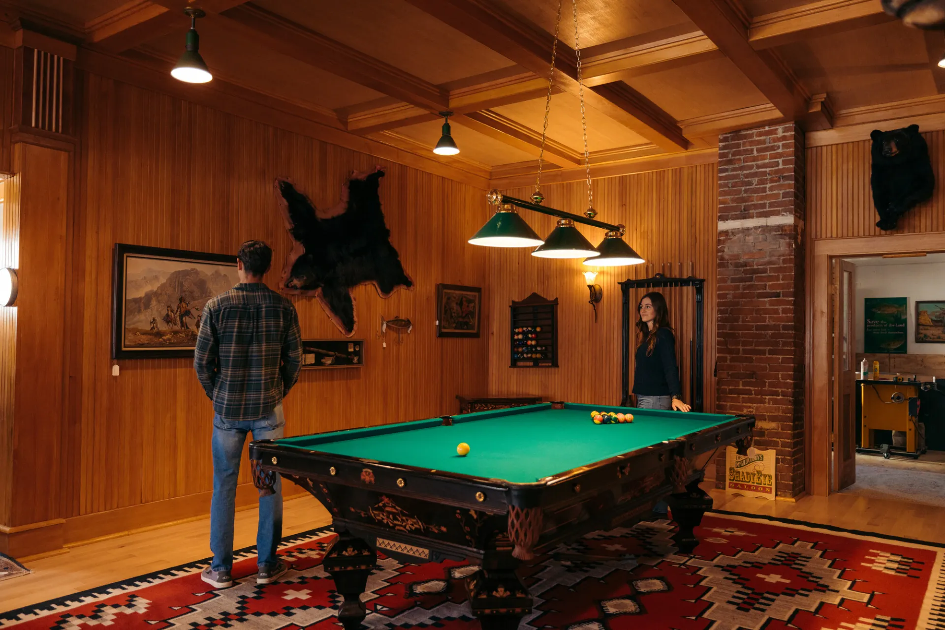 A man and woman look at a bear pelt on a wall.