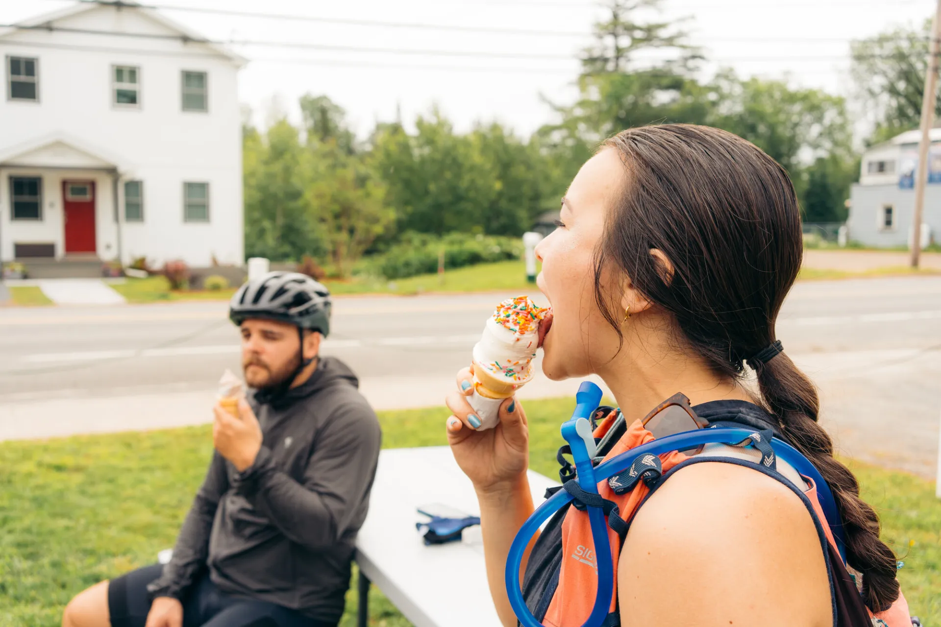 Two cyclists eat ice cream cones.