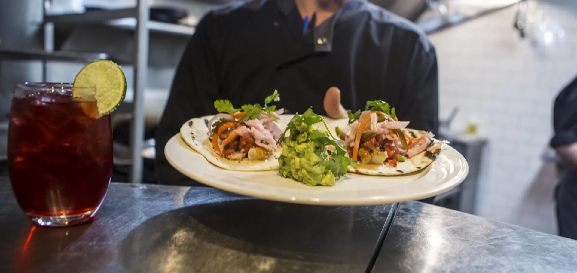 A server holds a plate filled with chicken tacos.
