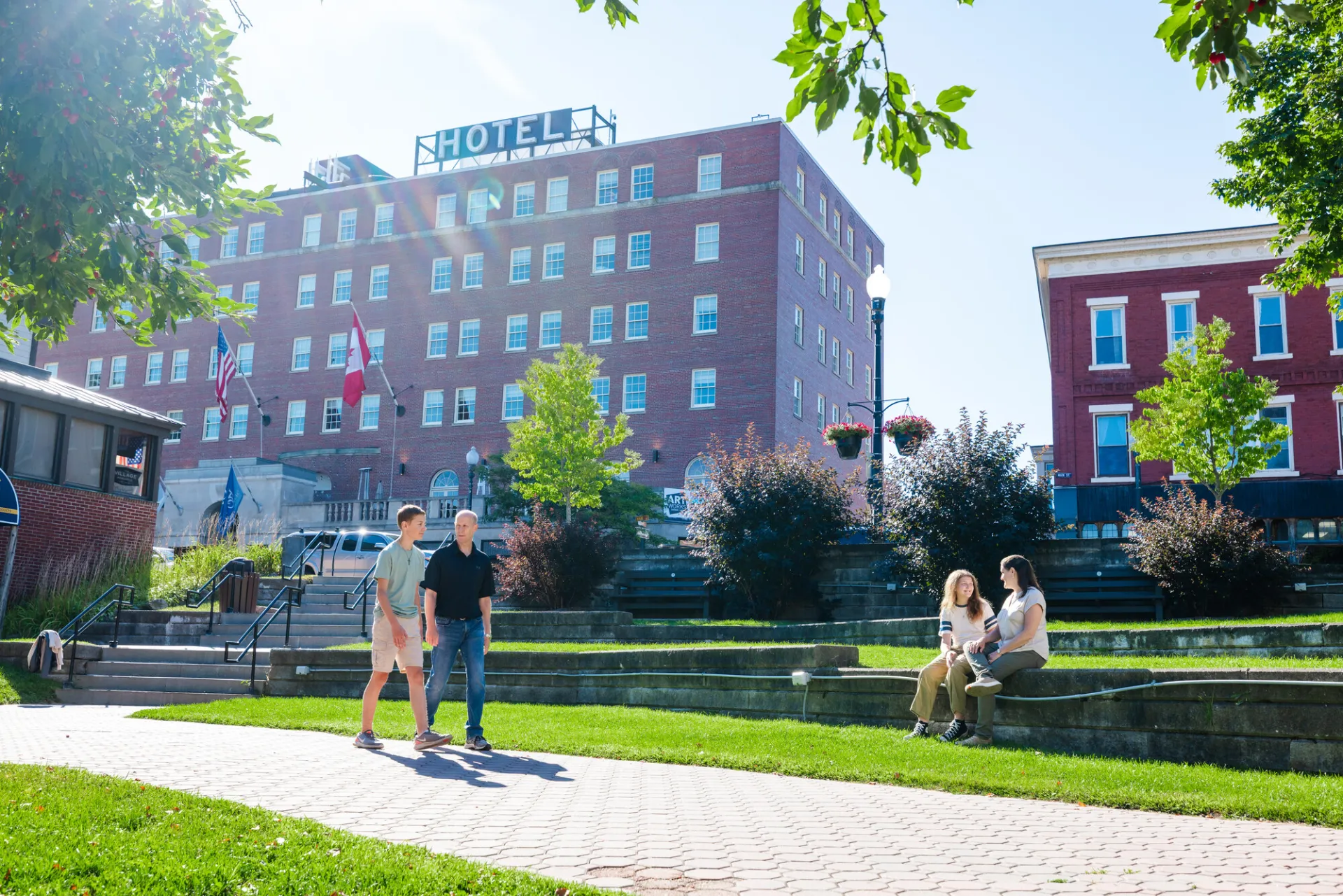 People play and walk in a park with a vintage hotel in the background. 