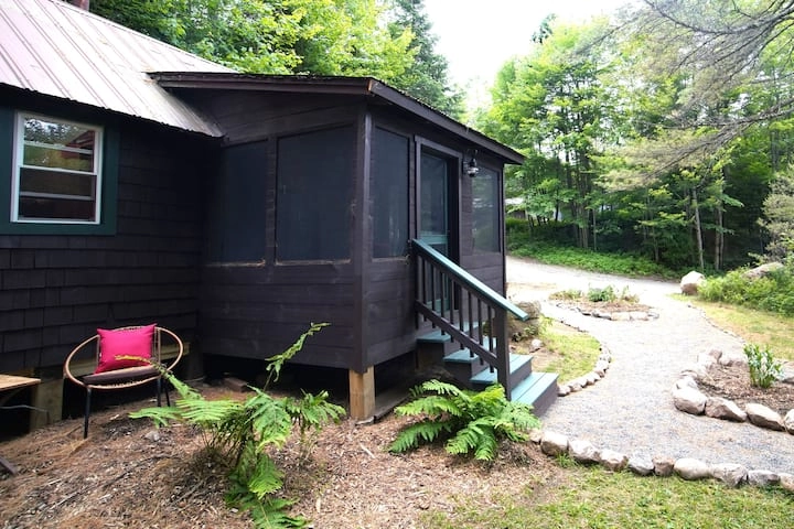 A dark brown cabin sits at the base of a driveway in the woods.