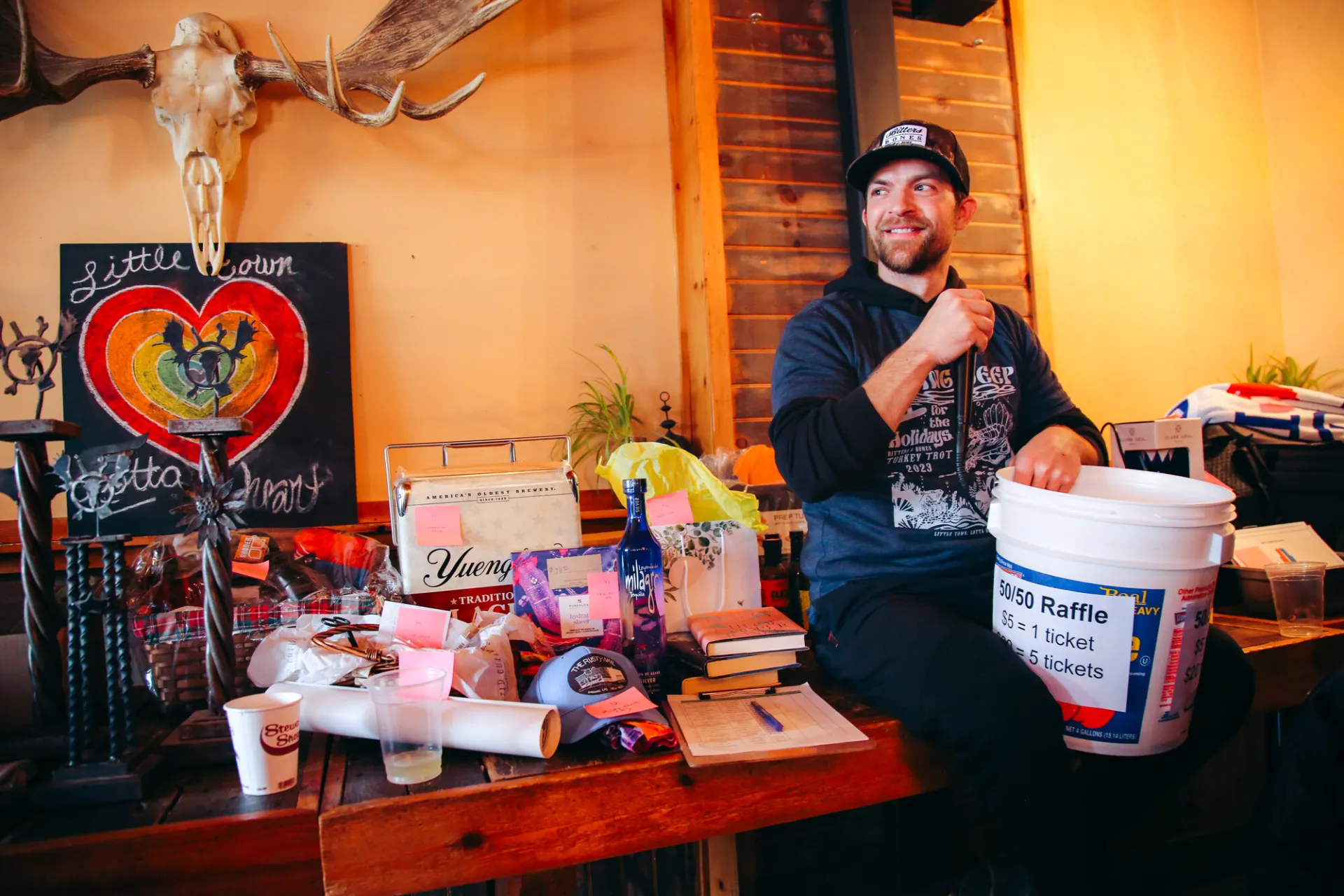 inside of bar with man seated on a table holding prizes and microphone 