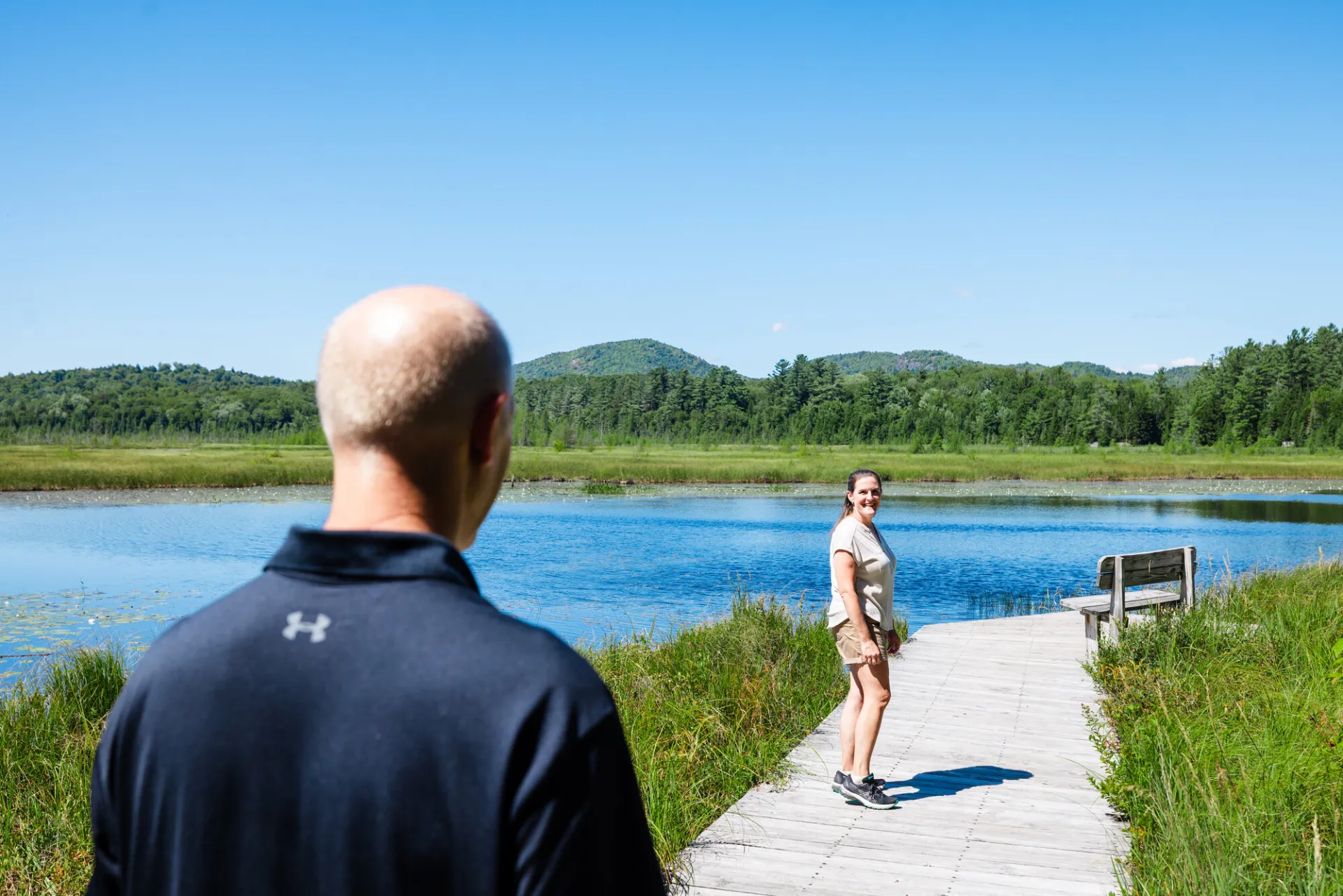 A man and woman walk on a walking path across marshland.