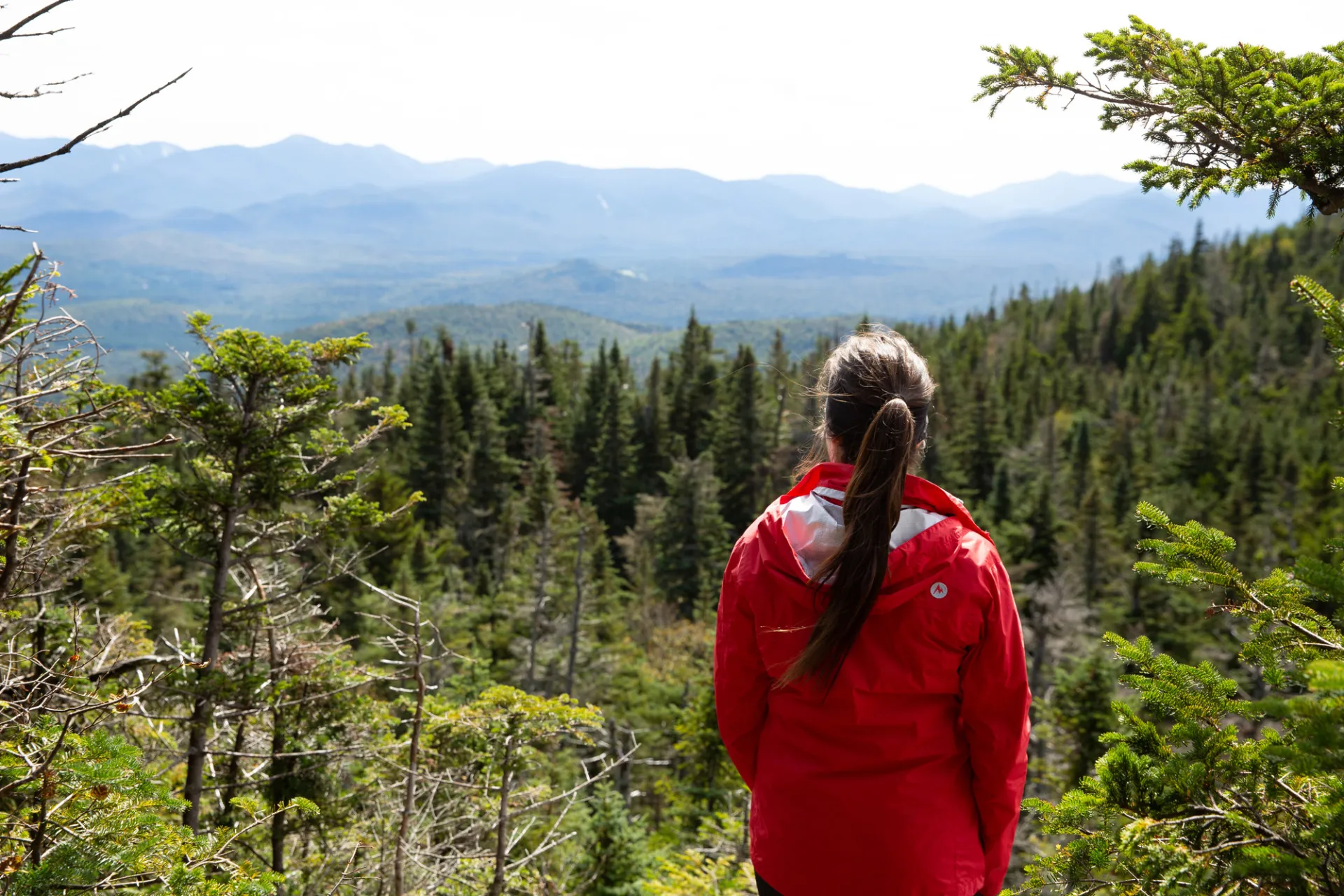 A woman in a red jacket looks out at a mountain range in spring. 