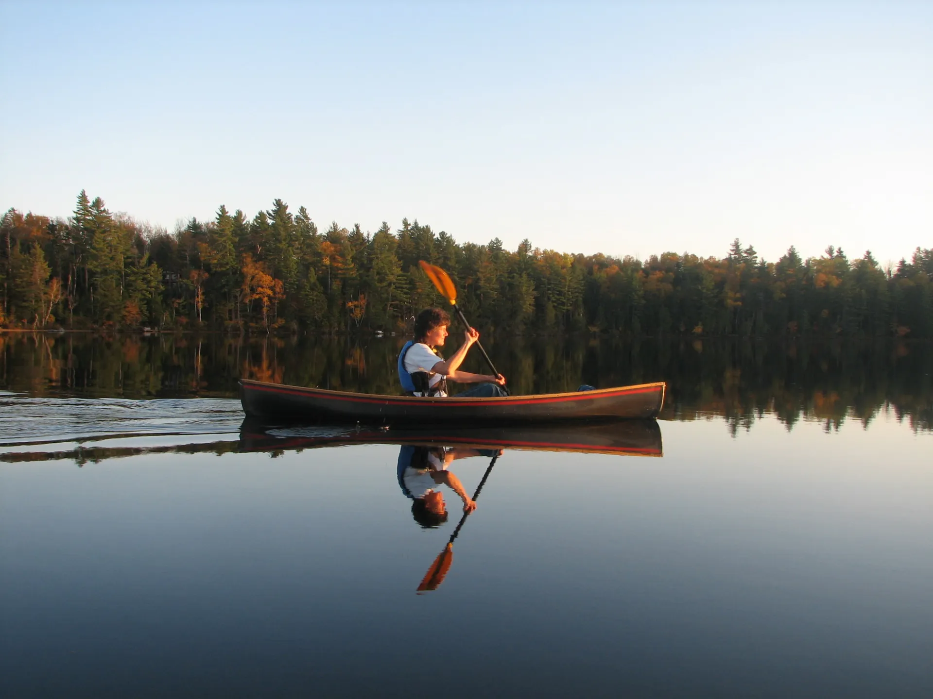 A person canoeing on a glassy lake during fall.