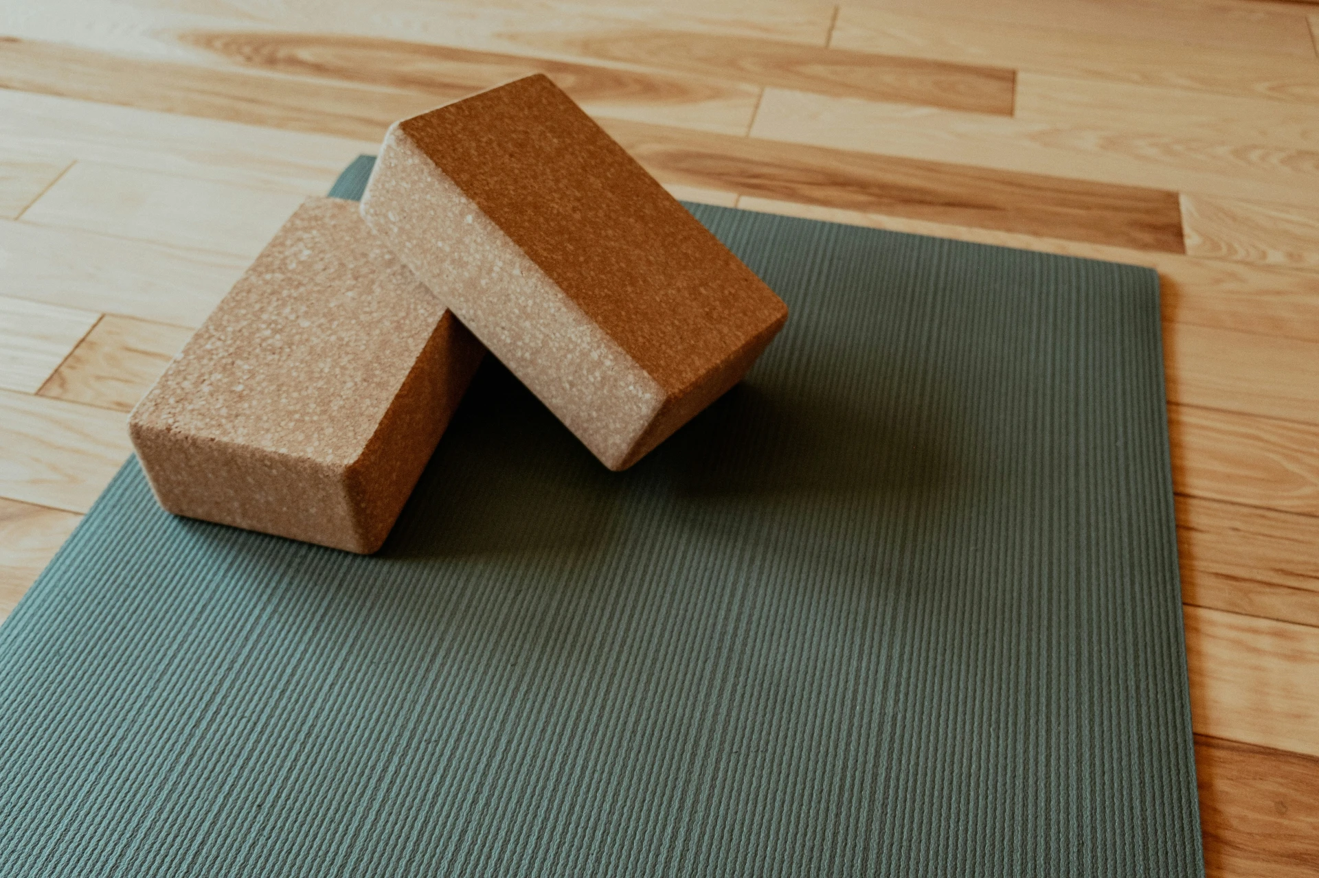 Two cork yoga blocks rest on a textured grey yoga mat spread across a light-colored hardwood floor.