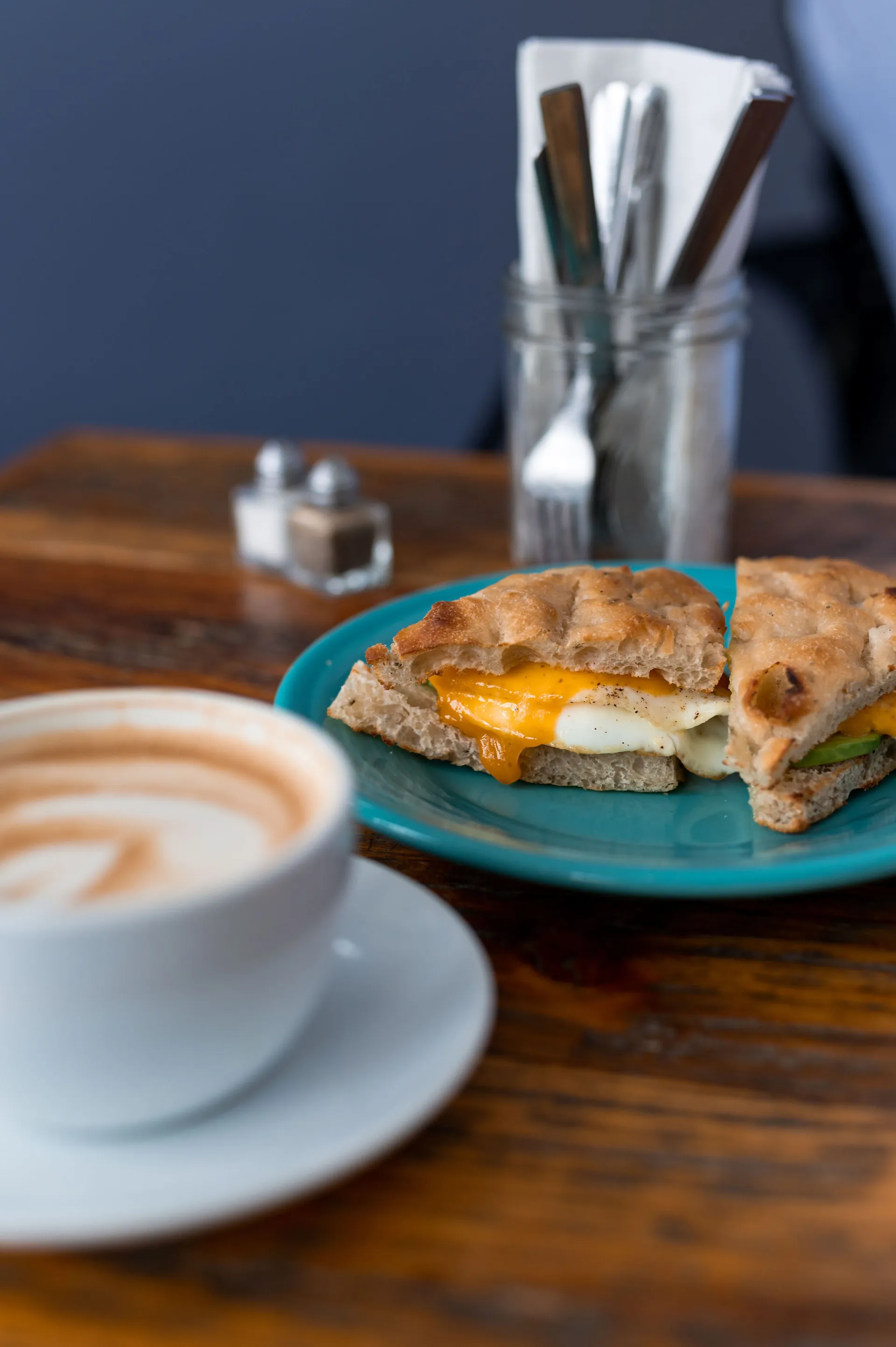 Egg sandwich on a fluffy english muffin next to a latte.