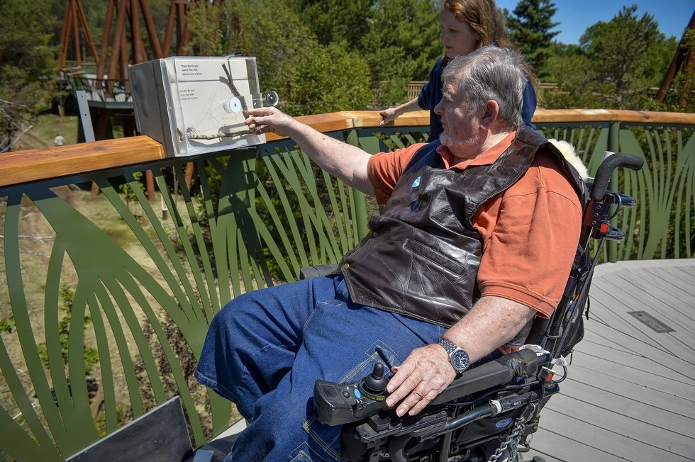 A man who uses a wheelchair stops along The Wild Walk to read a plaque