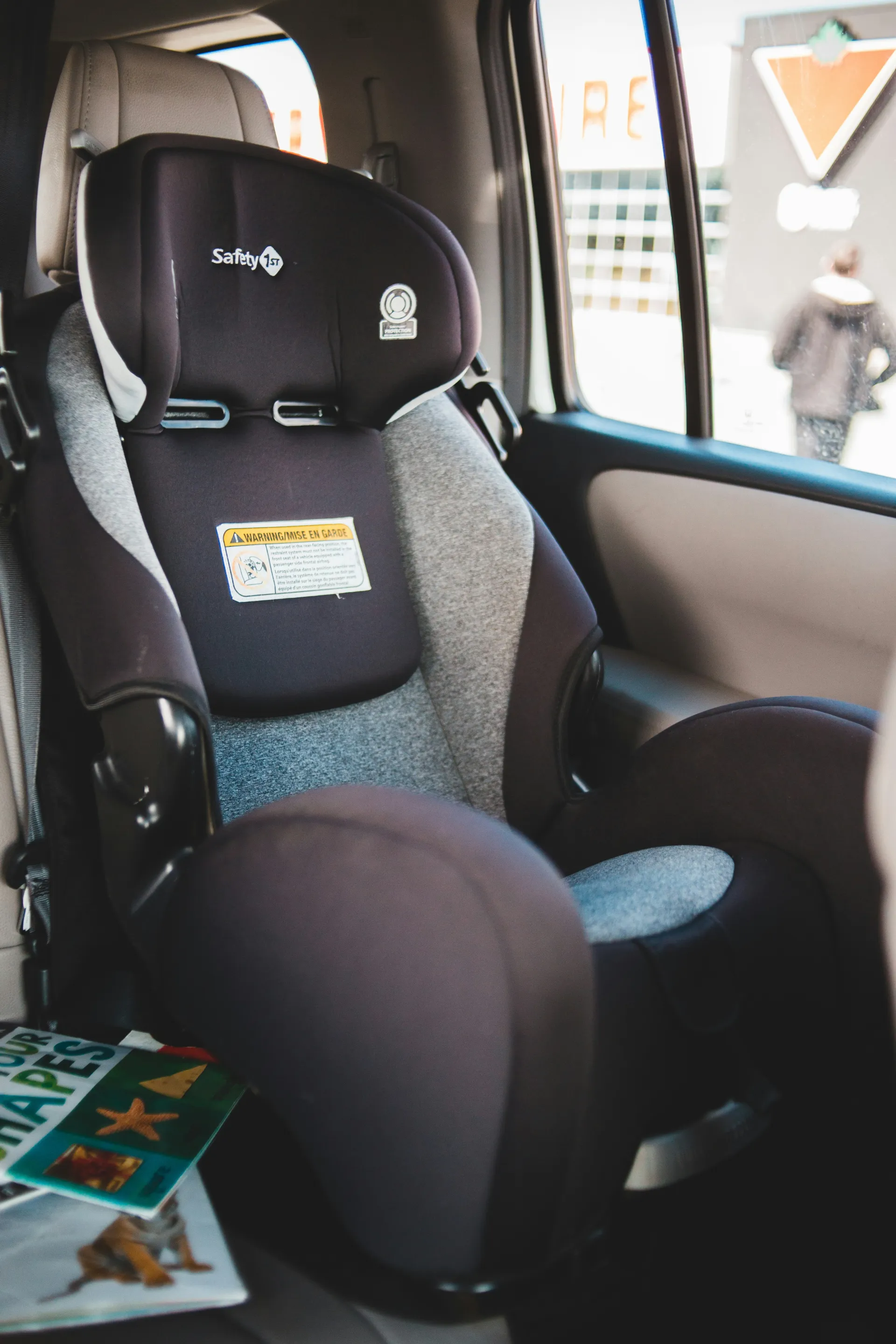 A black and gray Safety 1st car seat is installed in the backseat of a vehicle, with children's books resting next to it.