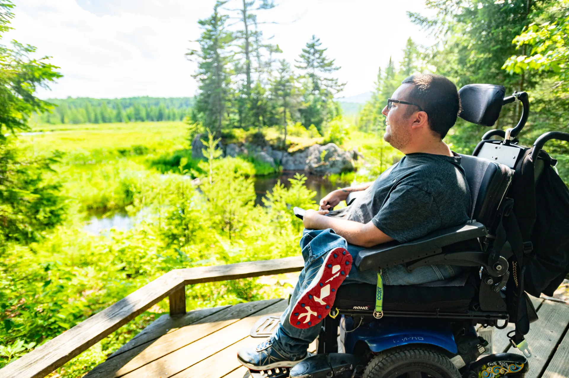 A man sits in a motorized wheelchair while looking out at marshland.