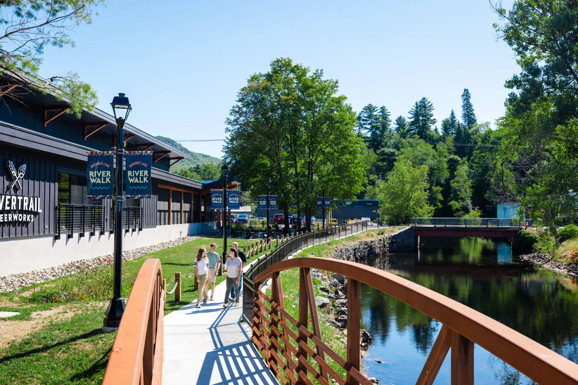 A family walks a trail along a river and brewery. 