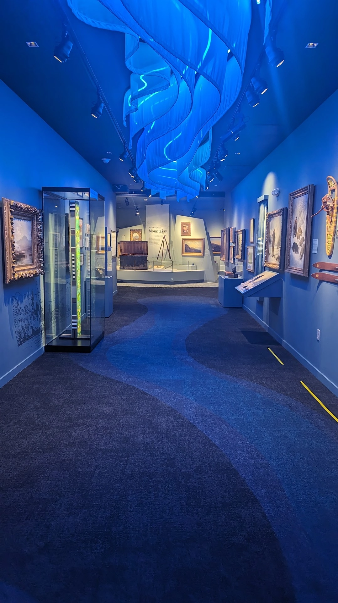 Art pieces on display in a long hallway with blue decor on walls, floor & ceiling which resembles waves.