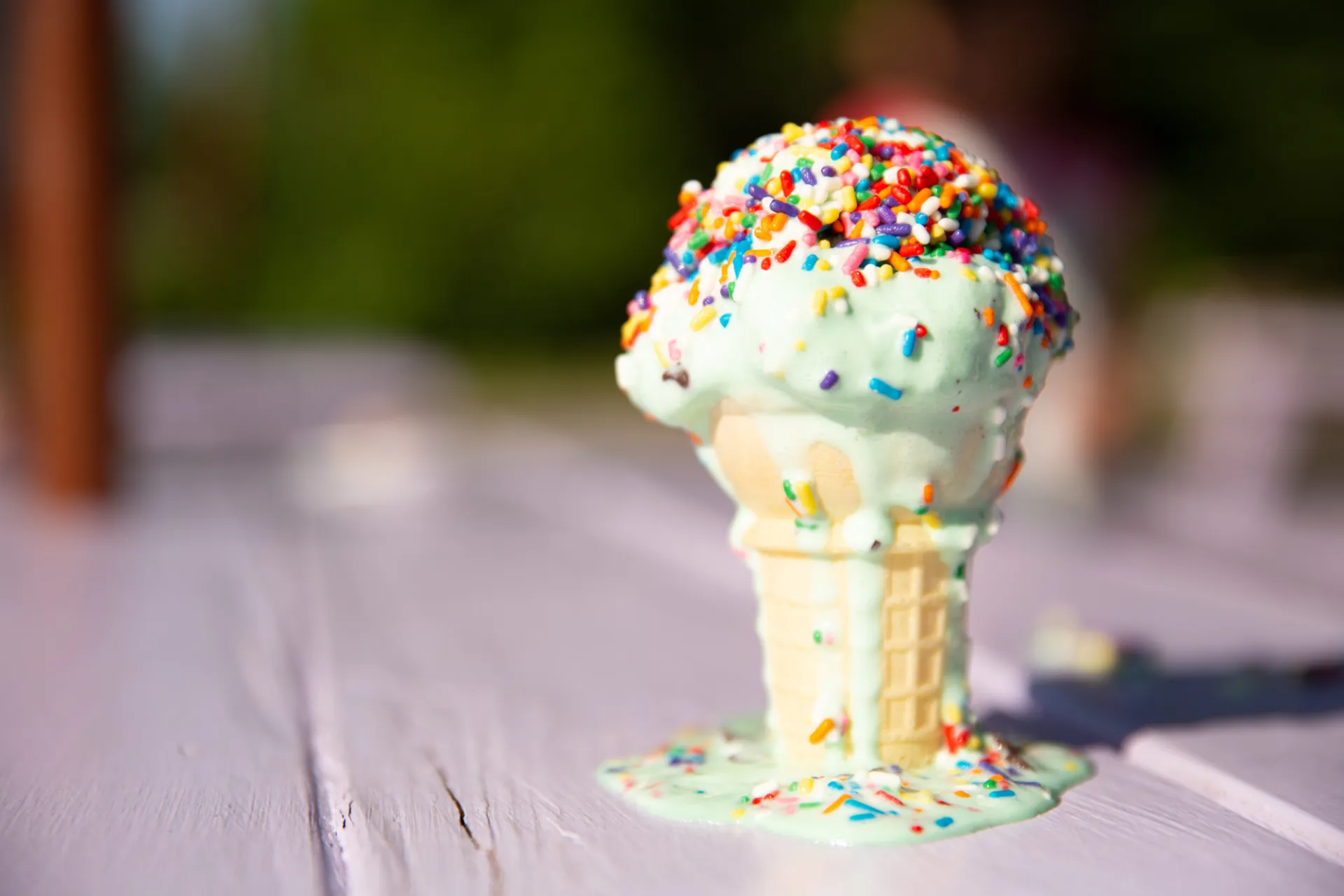 A close-up of a melting ice cream cone with sprinkles on a lavender table.