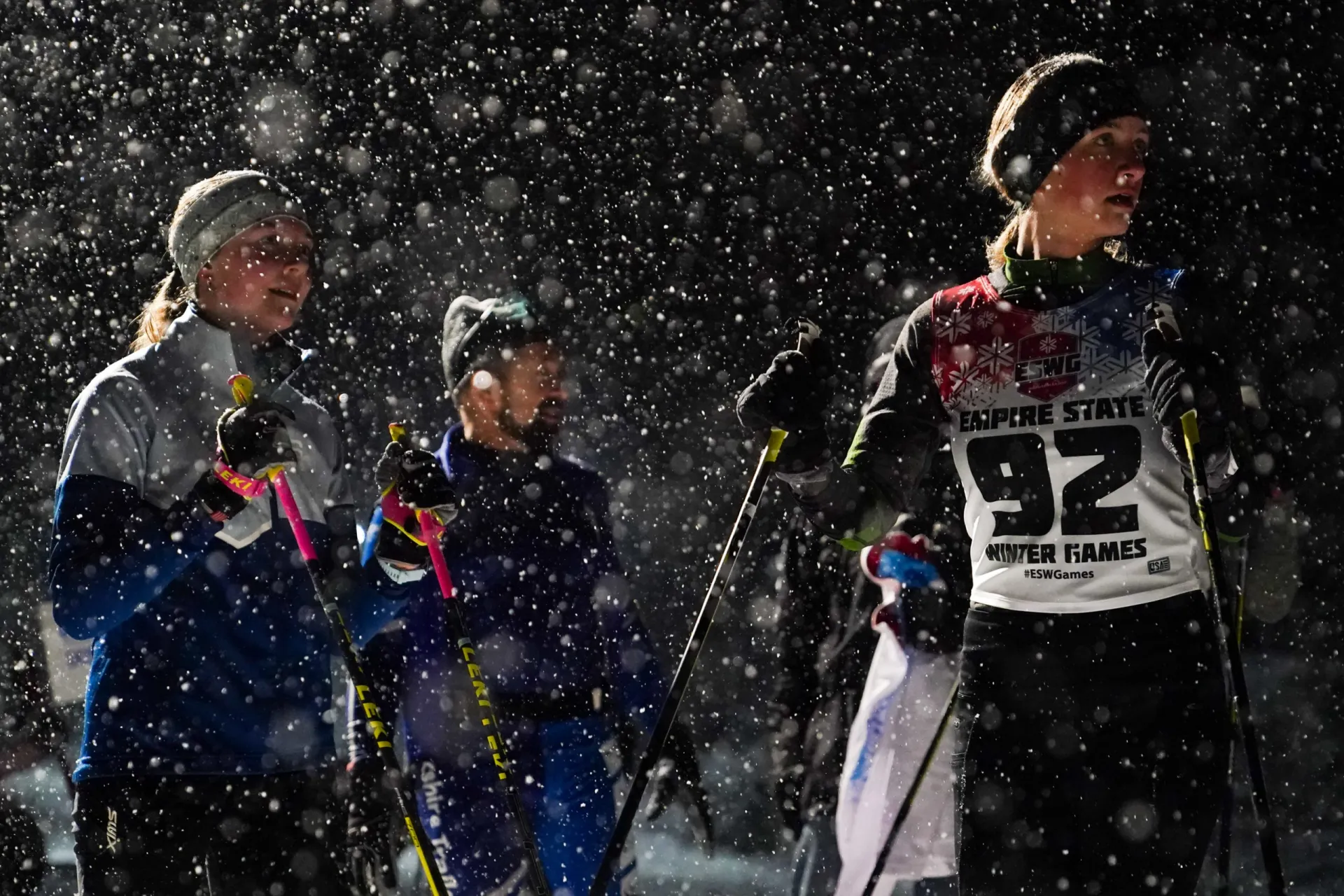 Athletes preparing for cross-country skiing in a snowy atmosphere at the Empire State Winter Games. Snowflakes fill the air.