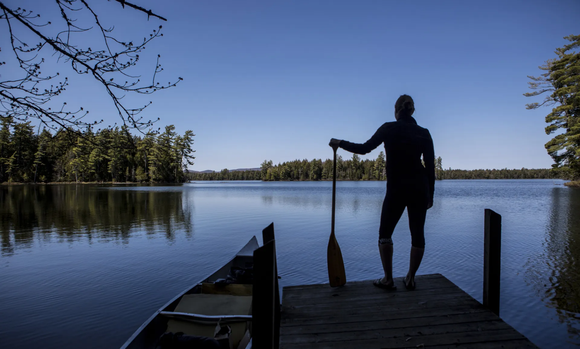 A paddler at the edge of a short, wooden dock by the water