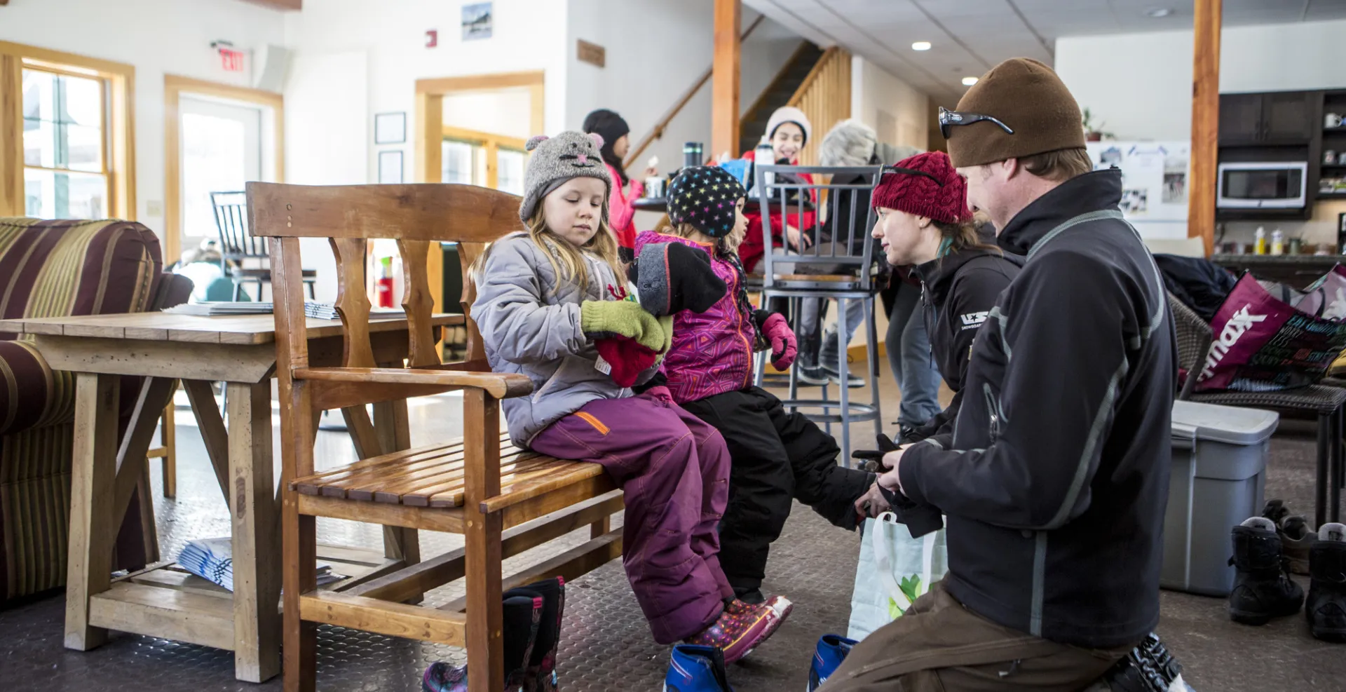 A father and mother help their kids put on ski boots as they sit on a bench inside the Dewey Mountain lodge.