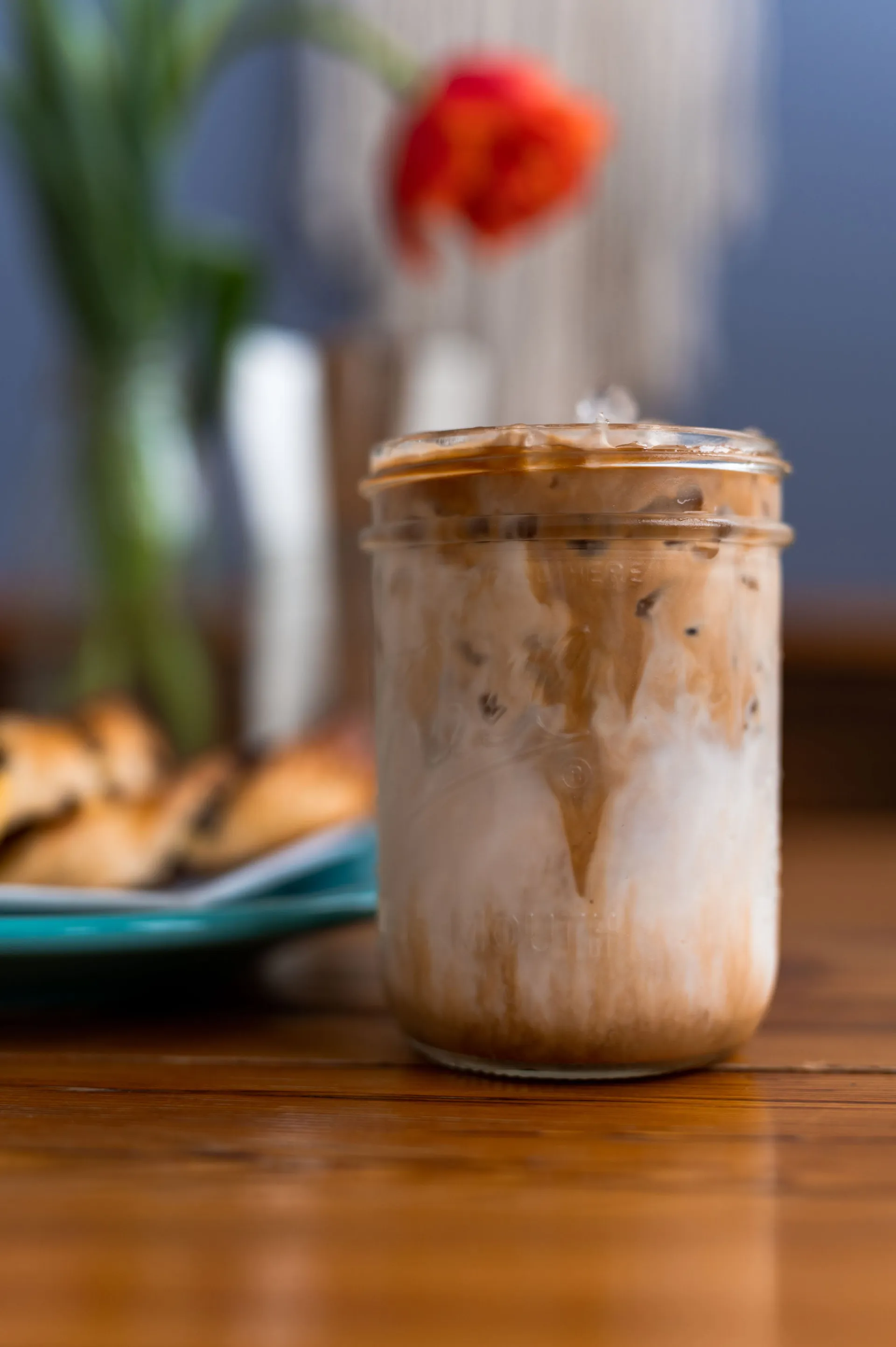 An iced coffee in a mason jar next to breakfast on a plate.