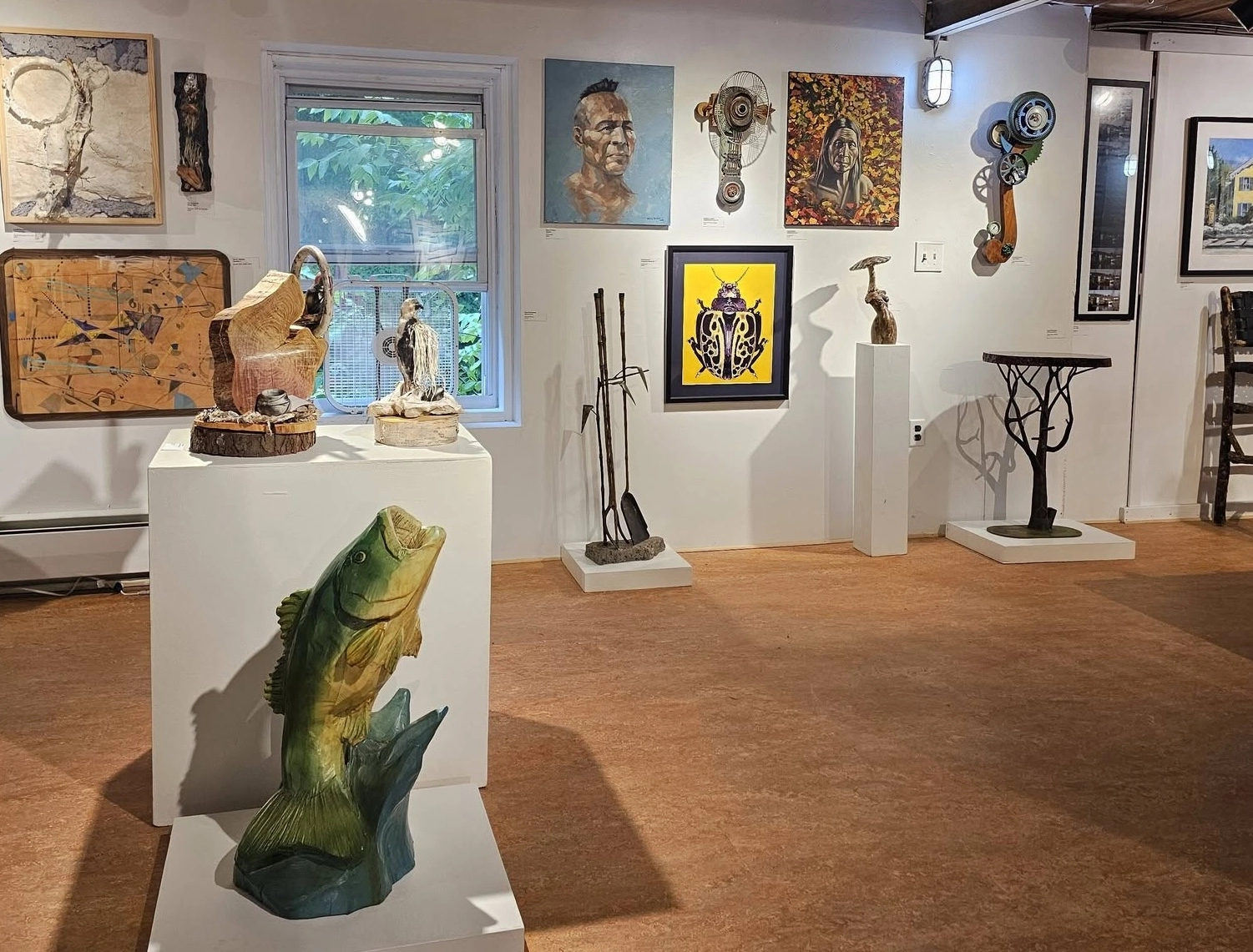 An art exhibit in a gallery with hardwood floors and rustic, exposed ceiling beams.
