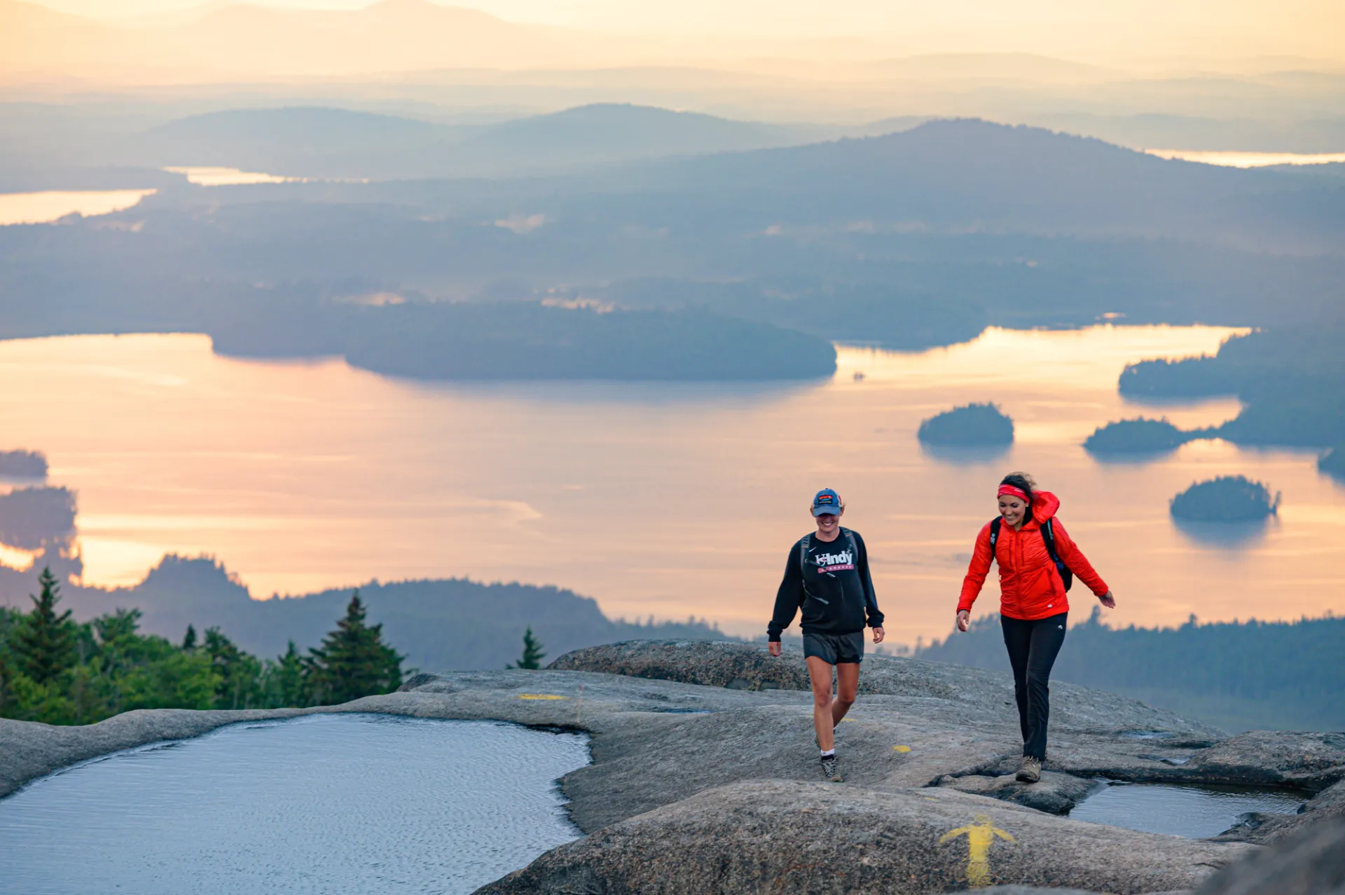 A couple people hiking Ampersand Mountain, a bare rock summit.