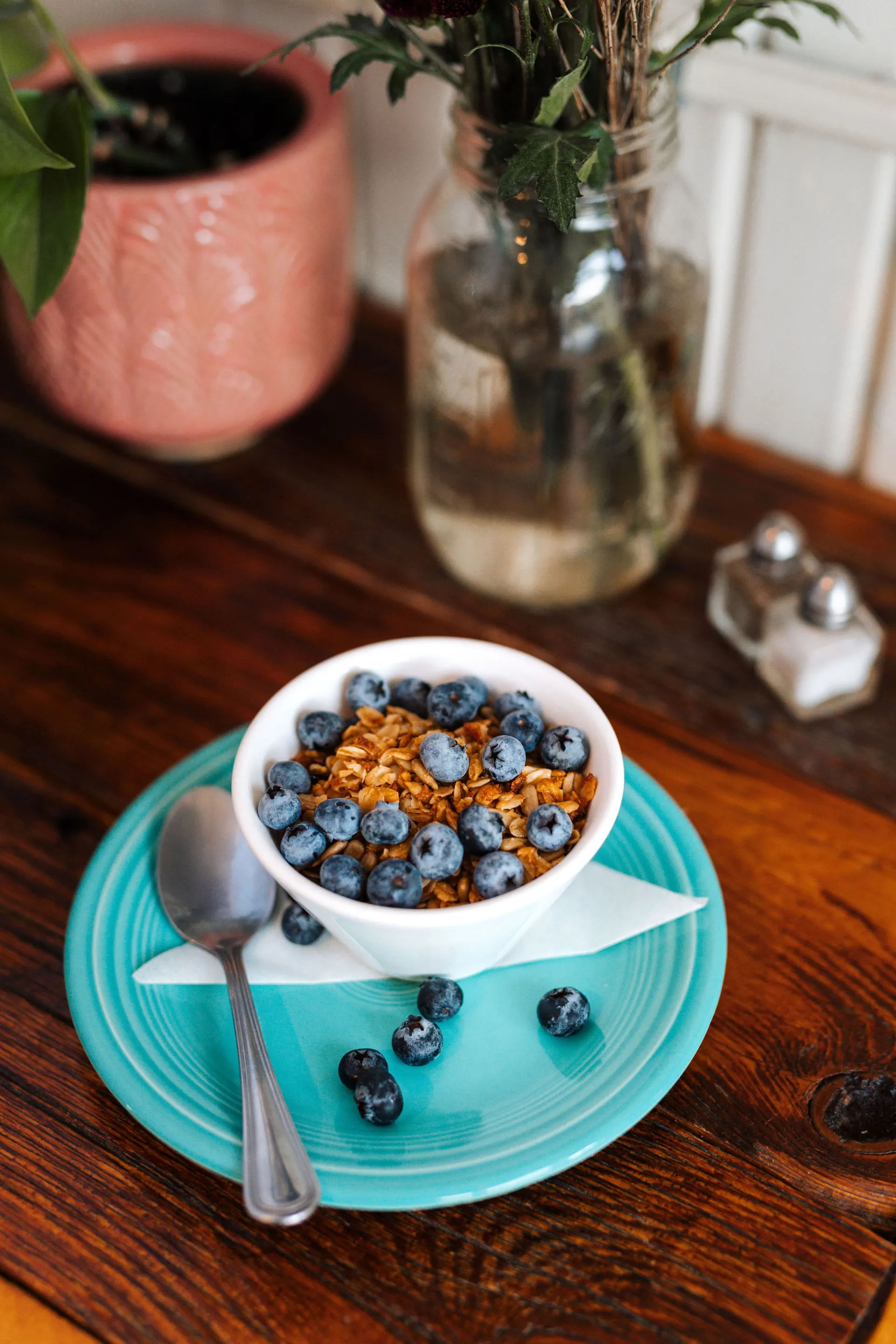 Berries and granola overflow their bowl onto the blue plate below the yogurt bowl.