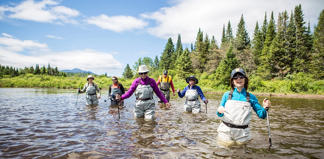 Smiling and laughing people walk the river in chest wadders