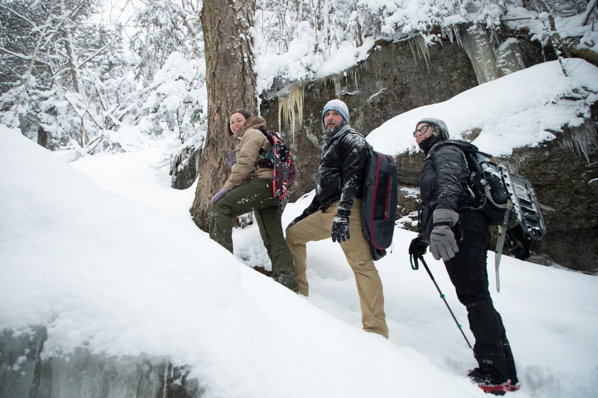 Three people smile while posing for a picture on a snowy hill on a hiking trail.