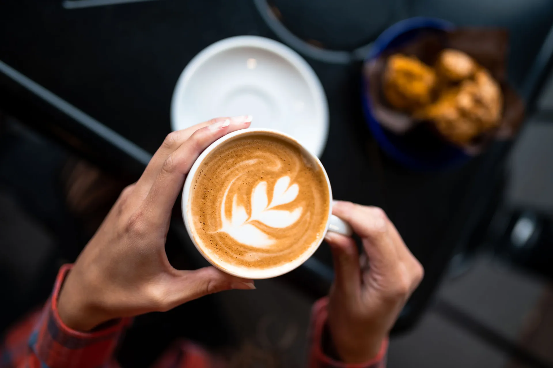 Hands holding a latte with art over a white saucer.
