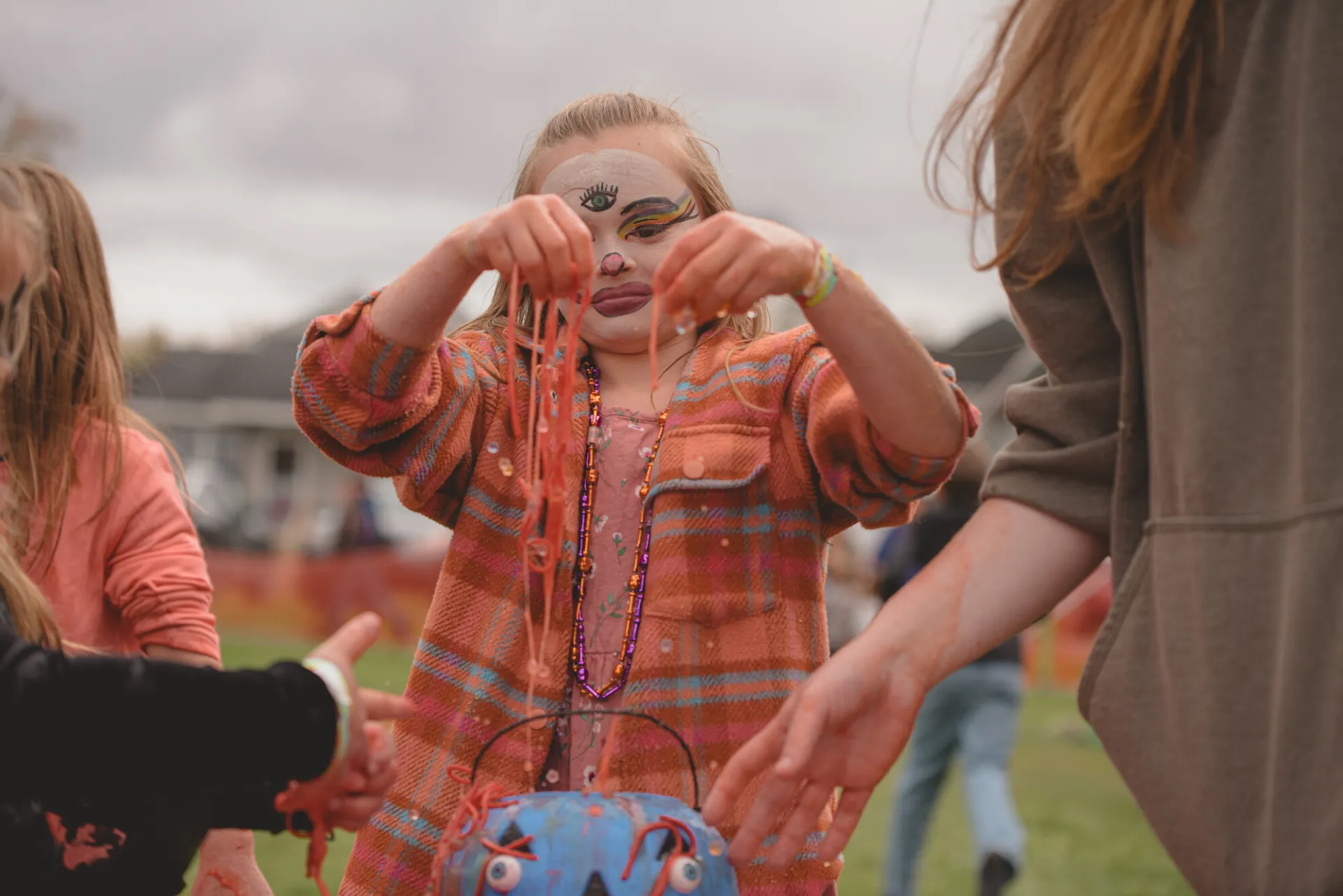 Child with face painted at Tupper's fall festival holds up necklaces.