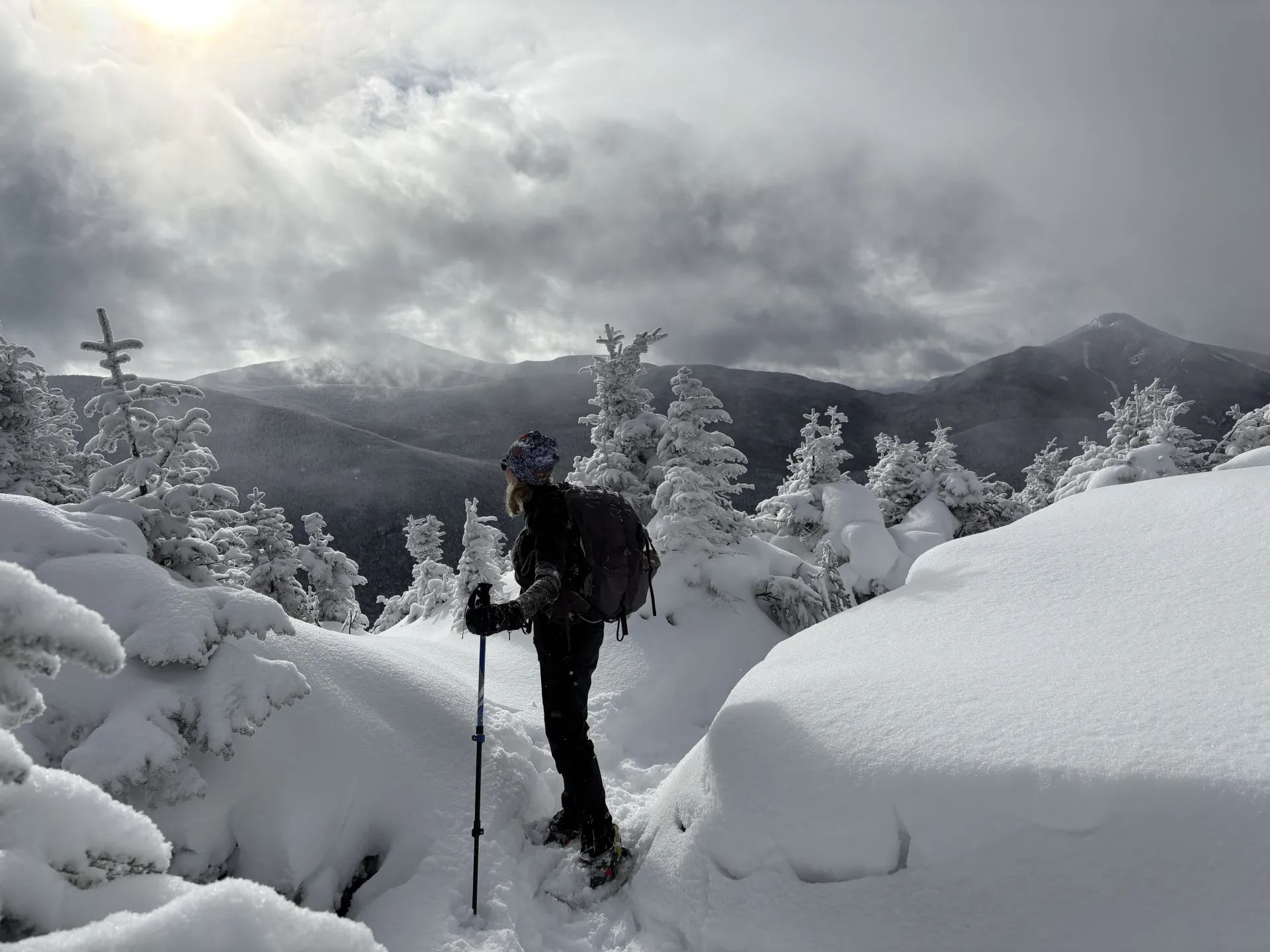 Snowshoer takes in the mountains in the distance, surrounded by pillows of beautiful snow and encrusted trees at the top of a peak