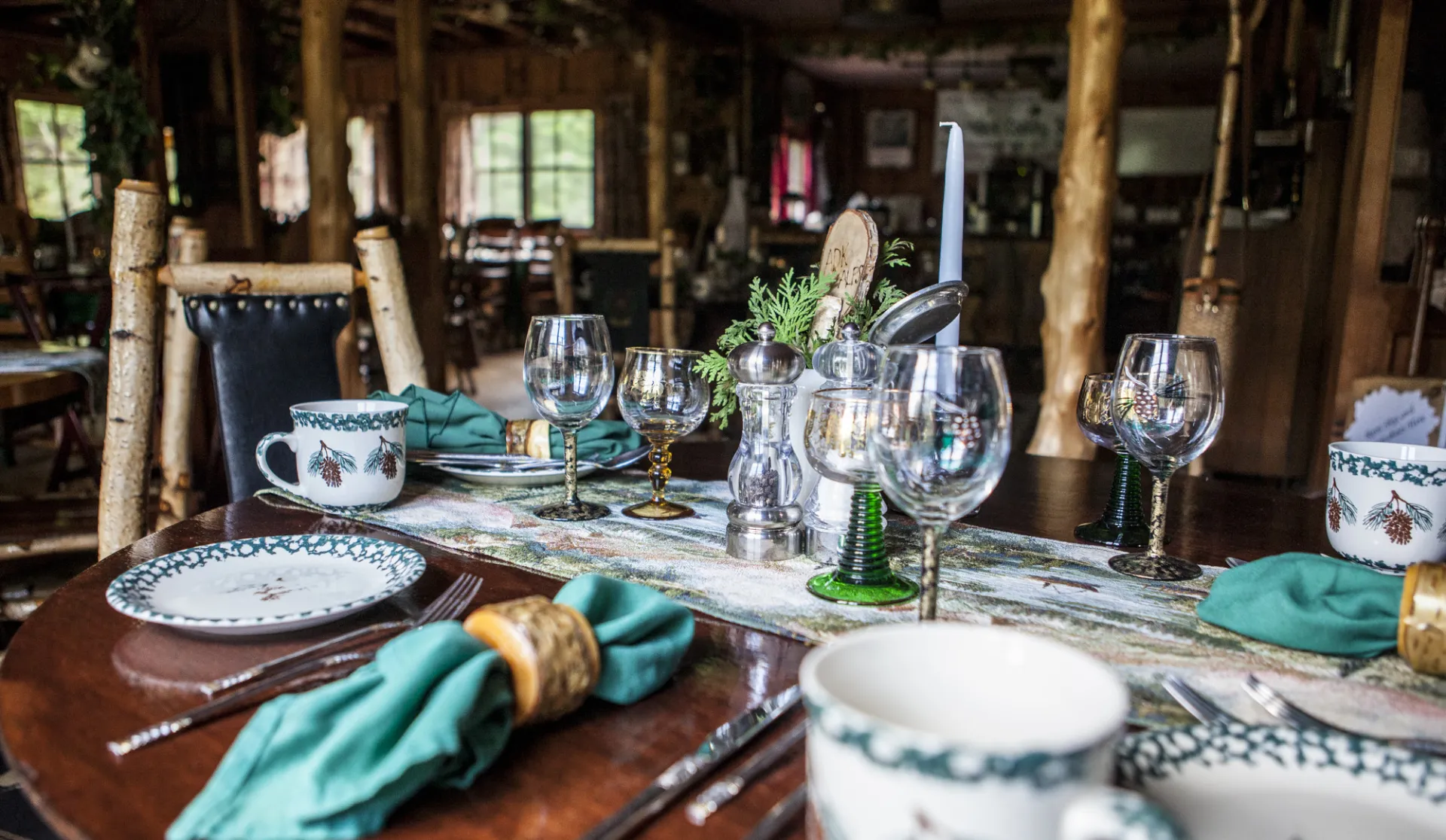 A dining table at a restaurant features rustic decorations, including green napkins and cedar greenery.