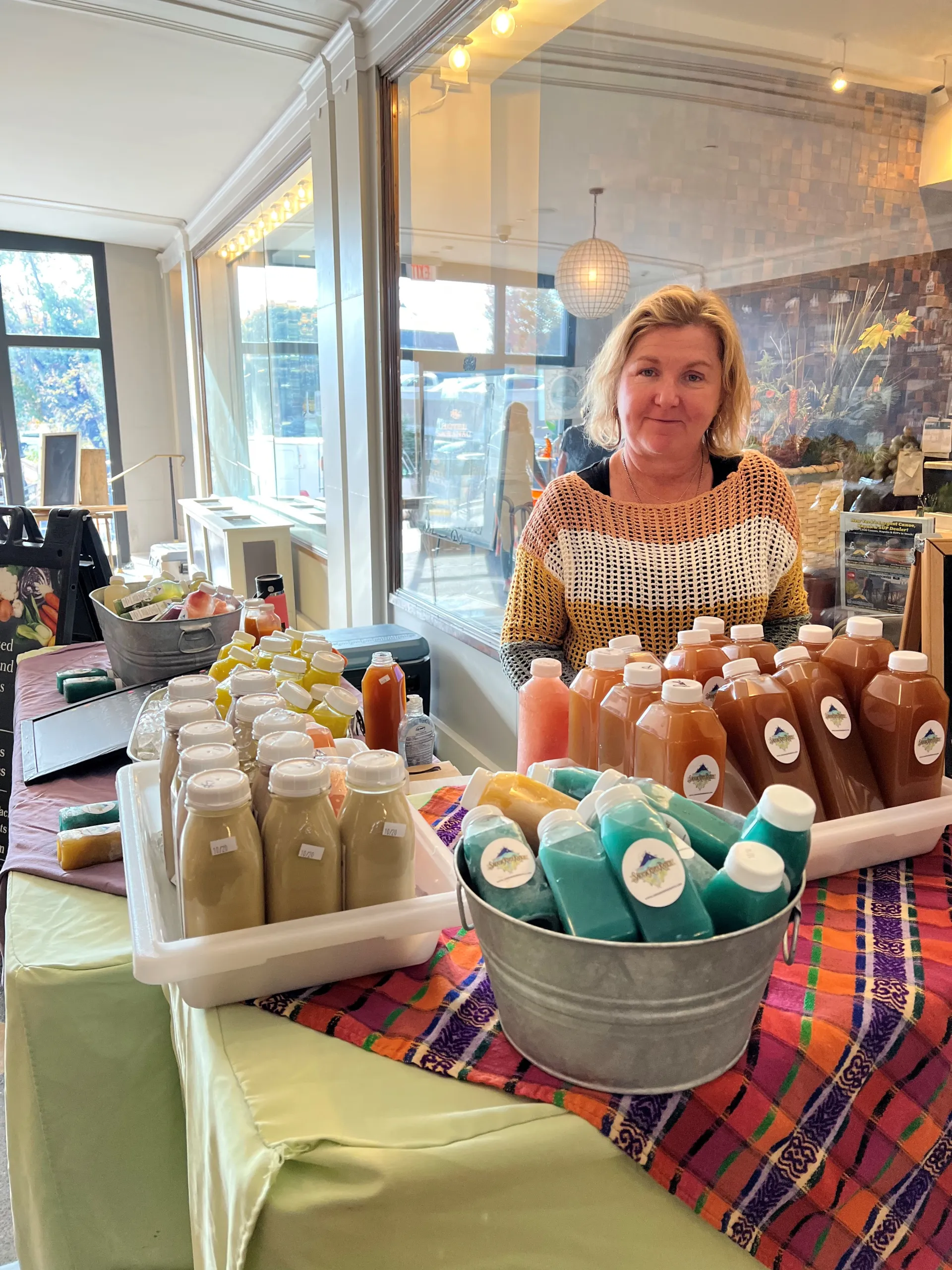 A woman mans a table at an indoor farmers market.