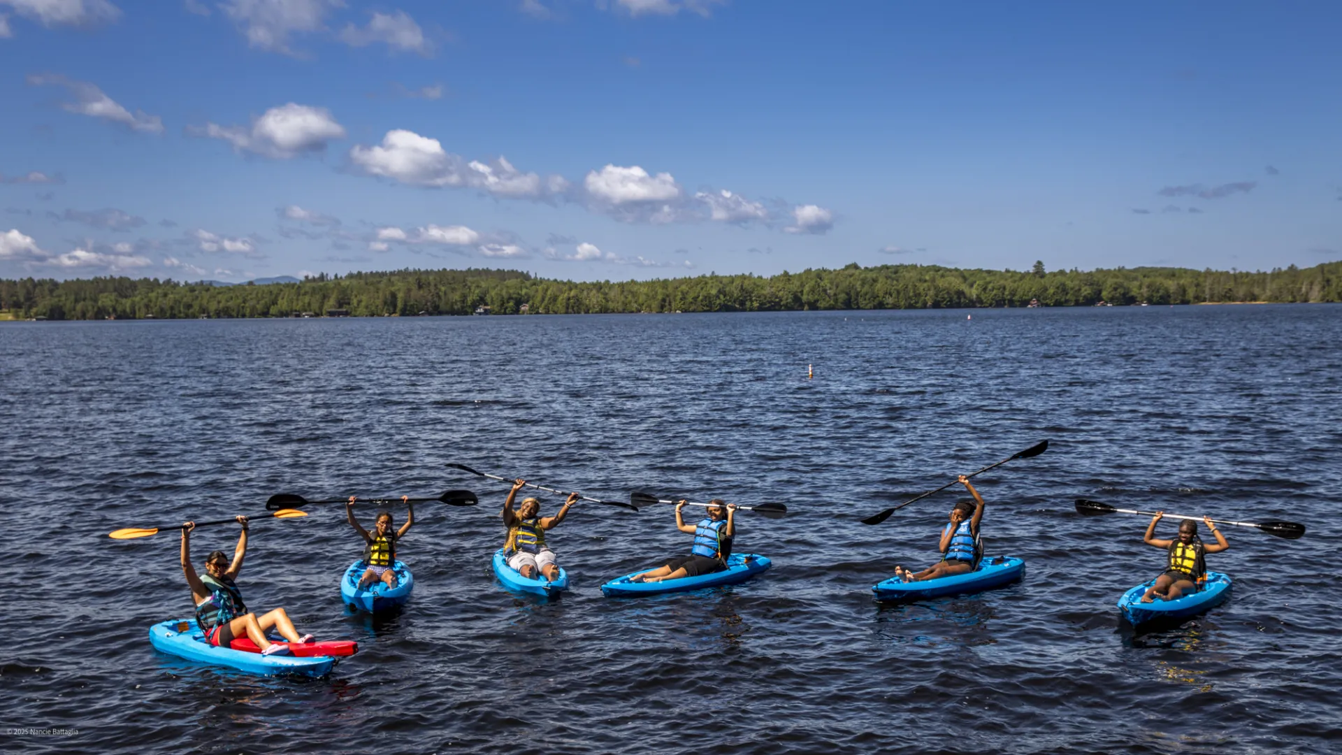 A group of kayakers hold their paddles above their heads in triumph.