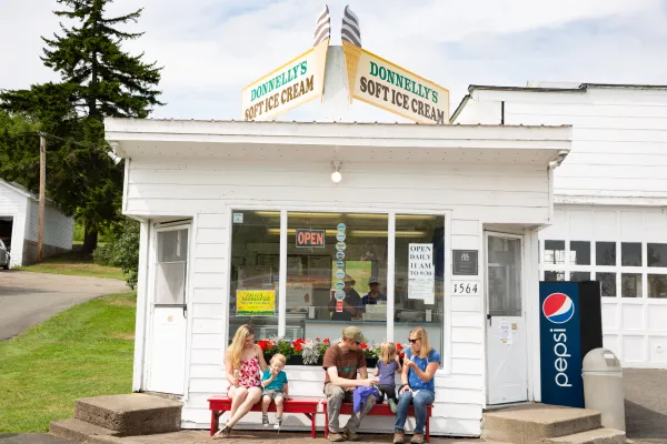 A family sits with ice cream in front of the small white building.