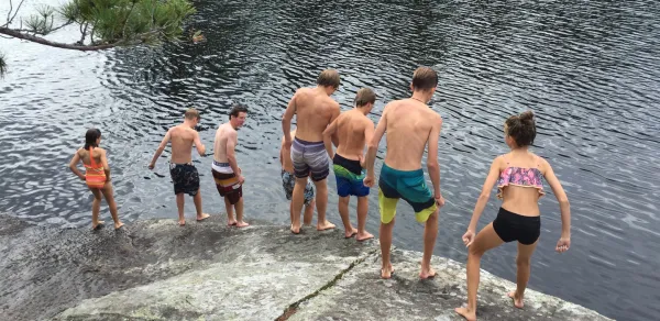 A group of boys stand on a rock while swimming.