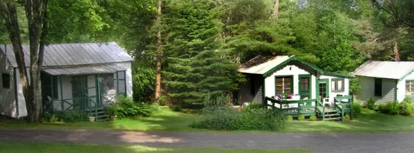 A white cabin with green trim surrounded by trees.