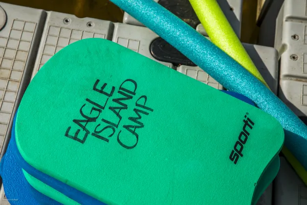 Colorful pool noodles and kick boards with Eagle Island Camp emblazoned.