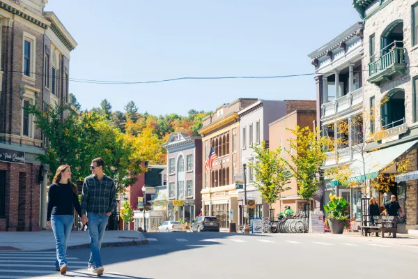 A man and woman cross the street in the downtown of a small town in fall.