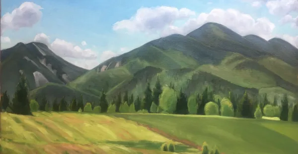 Rolling hills broken by stands of pines backed by tall mountains and blue sky.