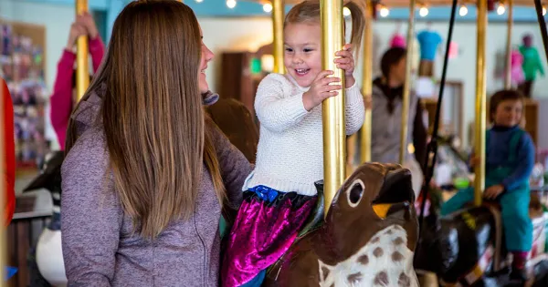 Mother holds daughter as she rides the carousel.